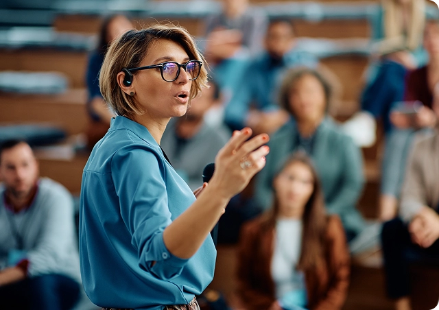 Moteris, sakanti kalbą universitete, ausyje turinti Vasco Translator E1 ausinę.