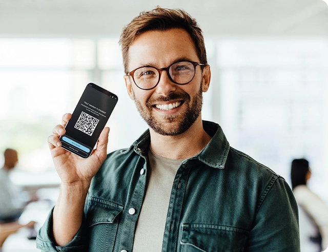 Besišypsantis vyras, laikantis išmanųjį telefoną su QR kodu, skirtu prisijungti prie Vasco Audience.