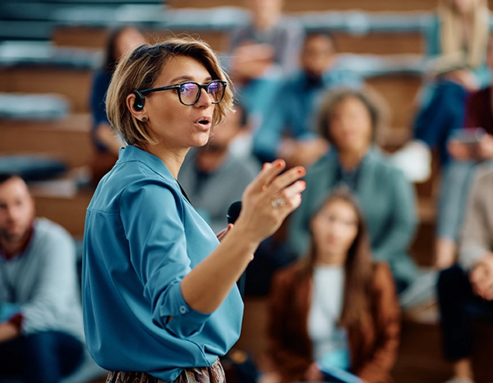Moteris, sakanti kalbą universitete, ausyje turinti Vasco Translator E1 ausinę.